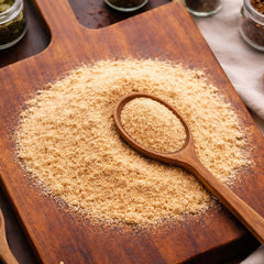 Fine cream-colored Maca Powder (Lepidium meyenii) on a wooden surface with a wooden spoon and herb jars in the background - CanadaVitaLife