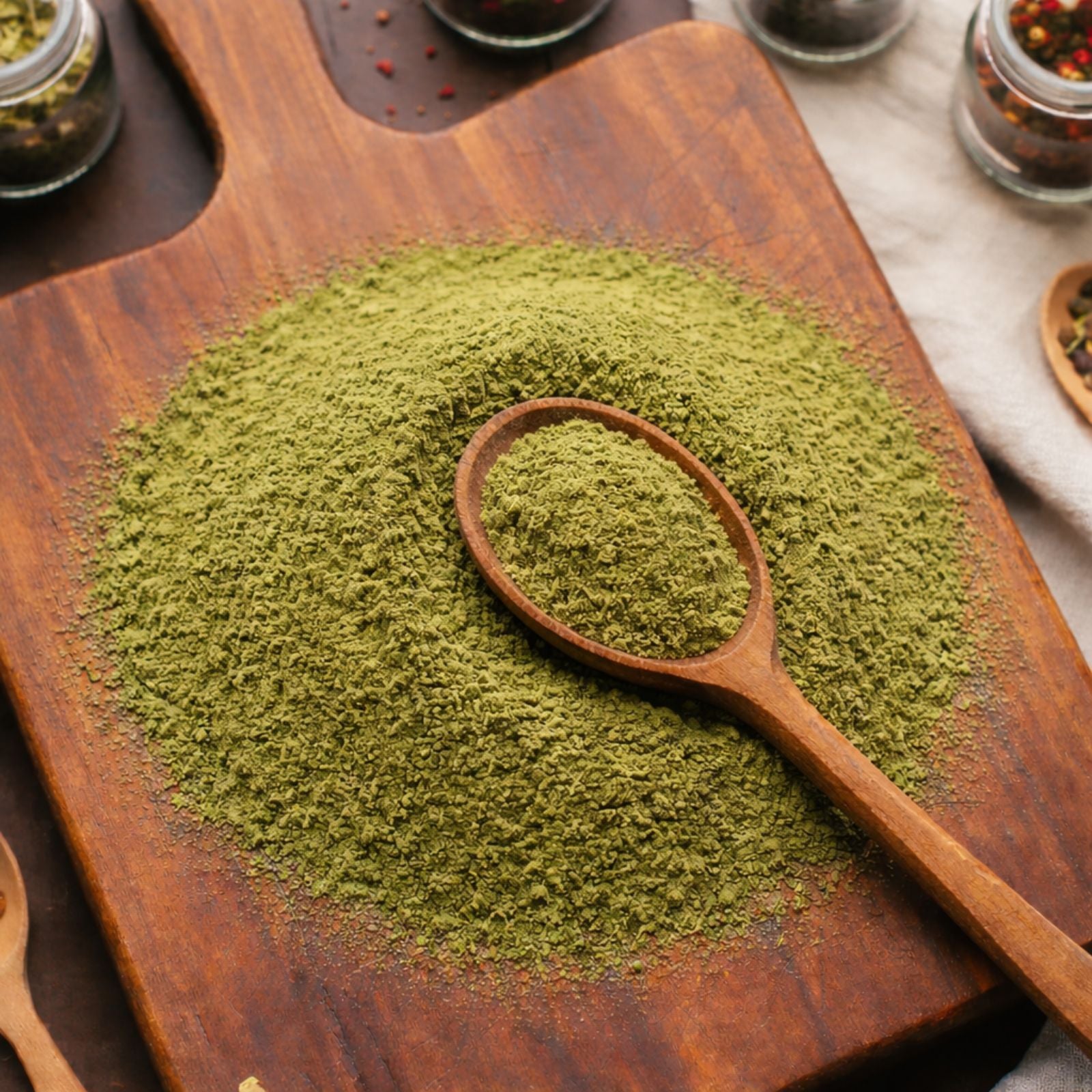 Fine green Spinach Powder (Spinacia oleracea) on a wooden surface with a wooden spoon and herb jars in the background - CanadaVitaLife