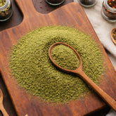 Fine green Spinach Powder (Spinacia oleracea) on a wooden surface with a wooden spoon and herb jars in the background - CanadaVitaLife